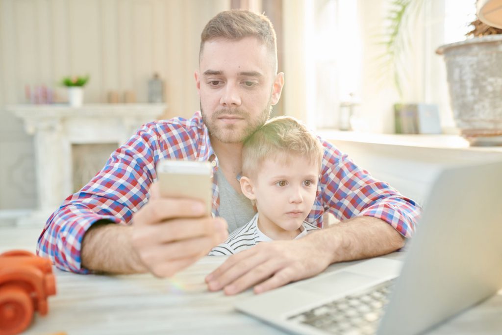 Warm toned portrait handsome young man sitting at working desk with son and calling by phone