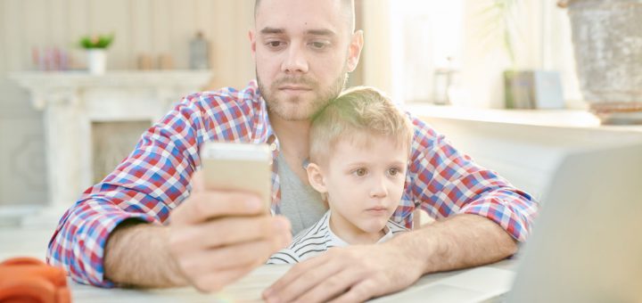 Warm toned portrait handsome young man sitting at working desk with son and calling by phone