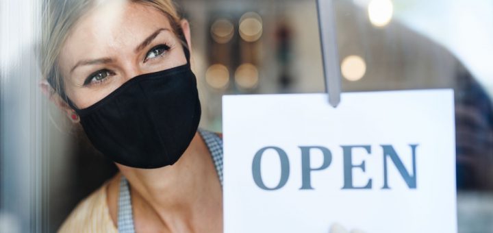 Coffee shop woman owner with face mask, open after lockdown quarantine. Shot through glass.