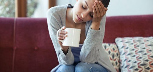 Shot of depressed young woman having headache while drinking coffee on sofa at home.