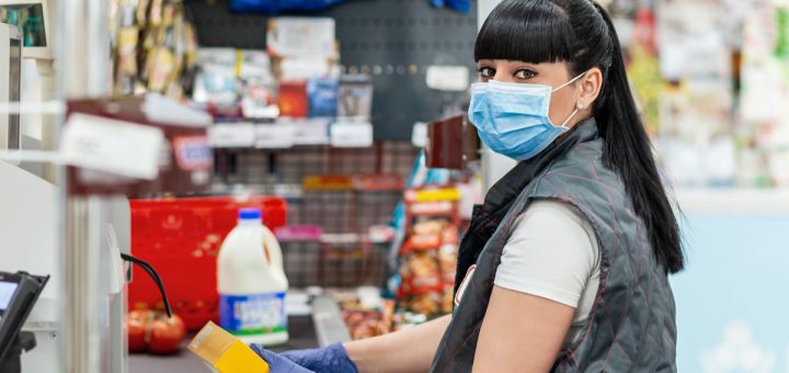 A portrait of young woman in a medical mask and gloves, working at the checkout in a supermarket. Concept of coronovirus, protection from infection and industrial crisis.