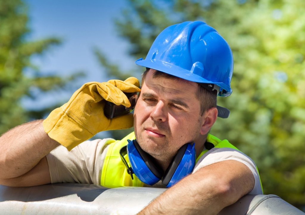 Tired worker with walkie talkie and safety equipment on oil plant