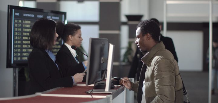 Two female airport security personnel checking identification at a check-in or boarding counter at the departure terminal holding the passports of two male passengers