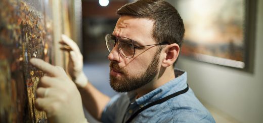 Man wearing gloves adjusting painting on wall; organizing in the culture sector concept