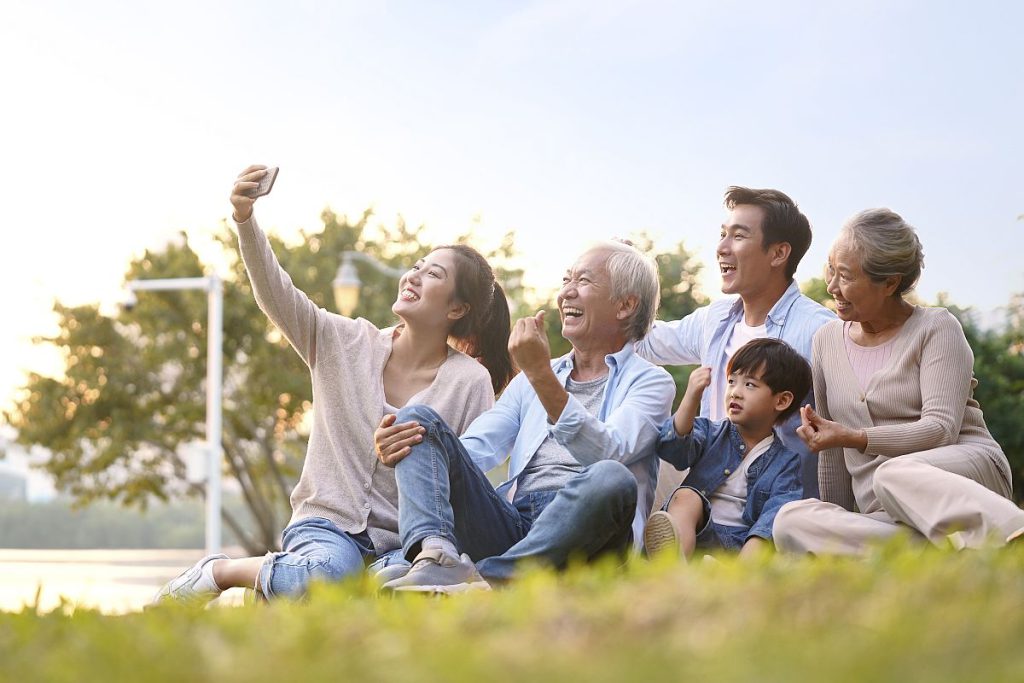 Three generations of a happy family sitting outdoors, taking a selfie; family benefits concept