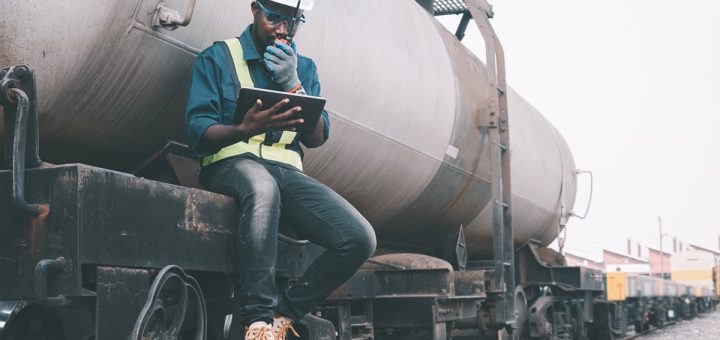 Engineer seated outside a train on a railway using walkie talkie and a tablet; rail unions concept