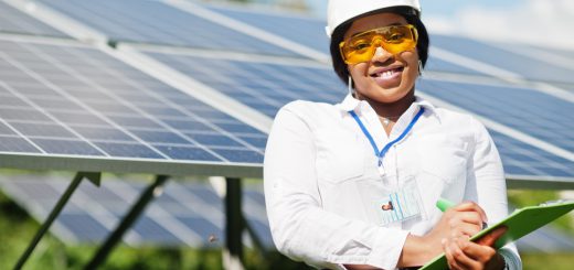 Woman wearing white hard hat, holding a tablet, stands in front of solar panels; Inflation Reduction Act benefits concept