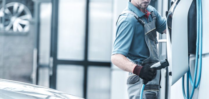 Worker plugging in electric vehicle; EV transition concept